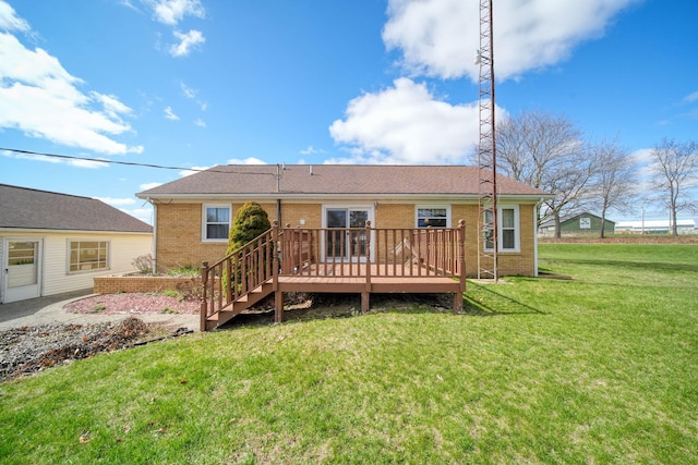 rear view of property with brick siding, a shingled roof, a deck, and a lawn