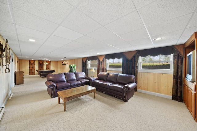living area with wood walls, baseboards, a paneled ceiling, and light colored carpet