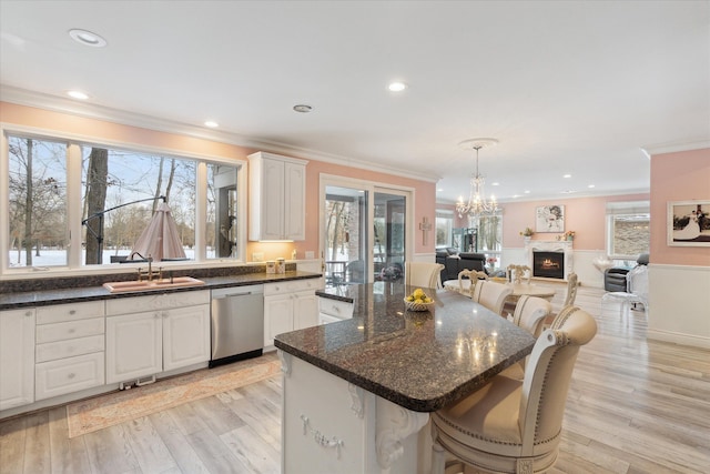 kitchen featuring crown molding, stainless steel dishwasher, an inviting chandelier, a kitchen island, and a sink
