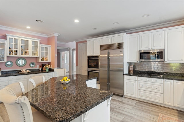 kitchen with glass insert cabinets, a center island, appliances with stainless steel finishes, decorative columns, and crown molding