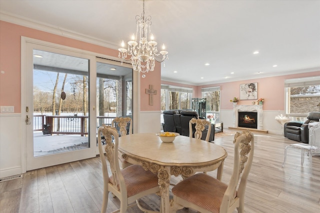 dining space with light wood-style flooring, an inviting chandelier, a fireplace, and ornamental molding