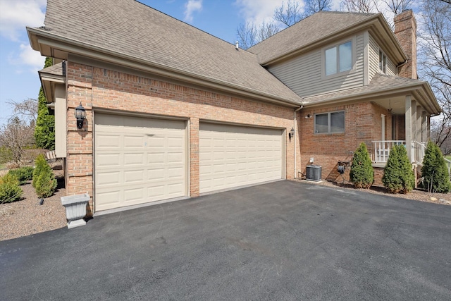 view of side of home with a chimney, driveway, an attached garage, brick siding, and central AC unit