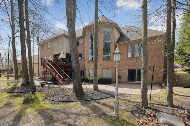 back of house with a wooden deck, a patio, brick siding, stairs, and a shingled roof