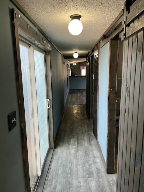 corridor with a barn door, a textured ceiling, and wood finished floors
