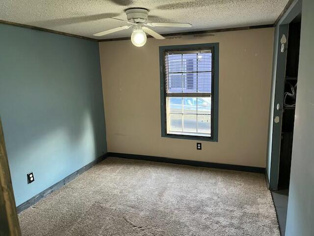 empty room with a textured ceiling, baseboards, a ceiling fan, and carpet