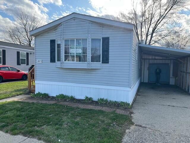 view of side of property featuring an attached carport, a lawn, and concrete driveway