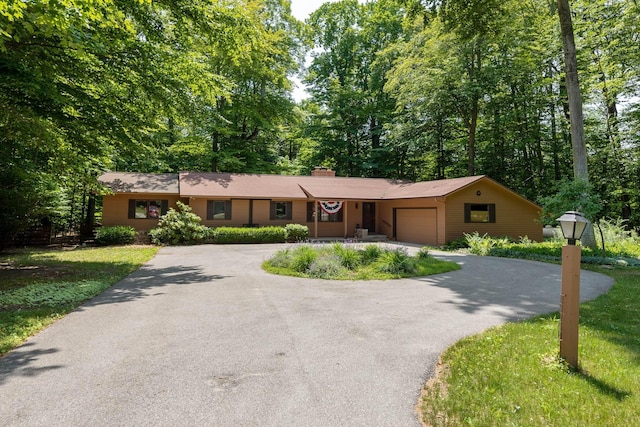 single story home with an attached garage, a chimney, and aphalt driveway