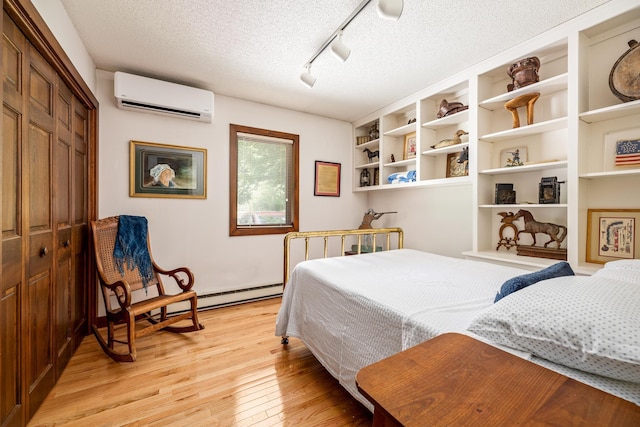 bedroom featuring a baseboard heating unit, a textured ceiling, light wood-type flooring, track lighting, and a wall mounted AC