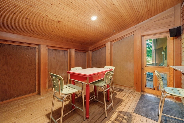 dining area with light wood finished floors, lofted ceiling, wood walls, and wood ceiling