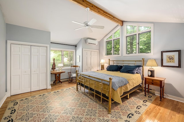 bedroom with a wall mounted air conditioner, multiple closets, vaulted ceiling with beams, light wood-type flooring, and baseboards