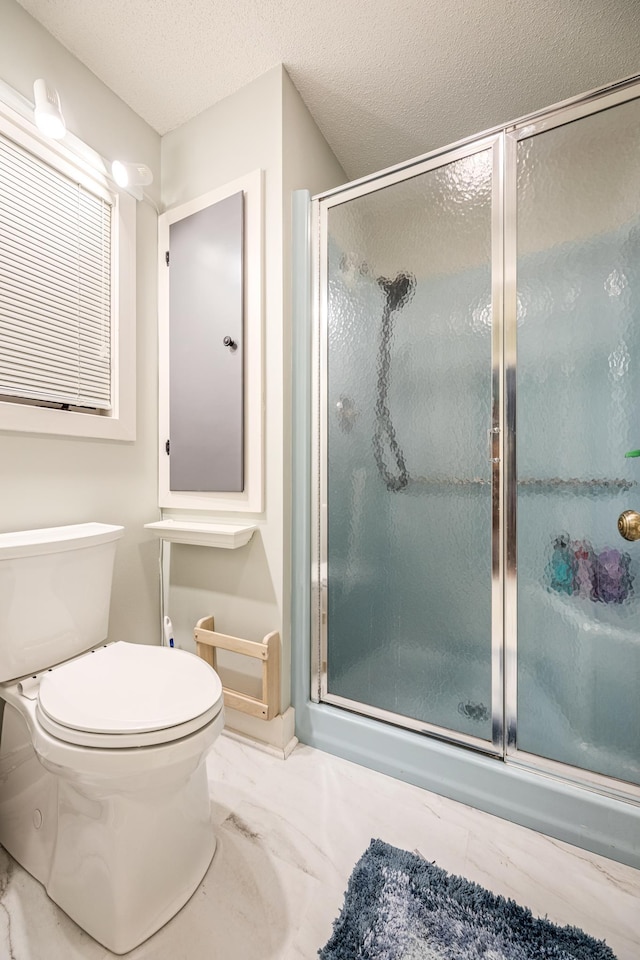 bathroom featuring toilet, marble finish floor, and a stall shower