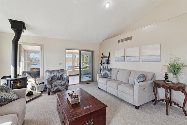 living area featuring visible vents, a wood stove, light carpet, and lofted ceiling