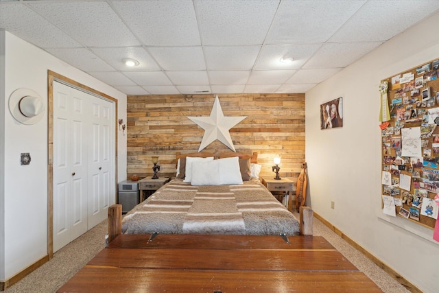 carpeted bedroom featuring a closet, wooden walls, a paneled ceiling, and baseboards