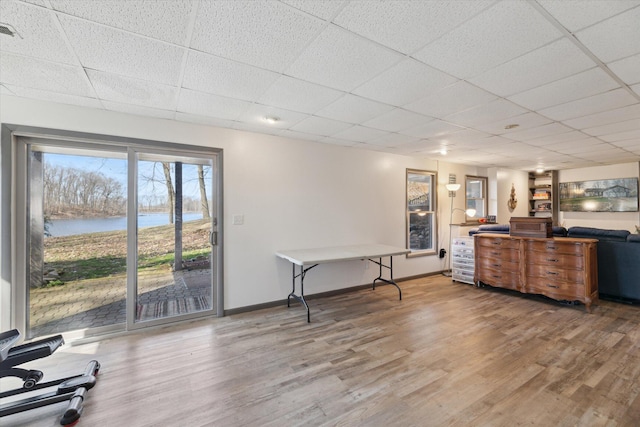 interior space with a water view, baseboards, a paneled ceiling, and wood finished floors