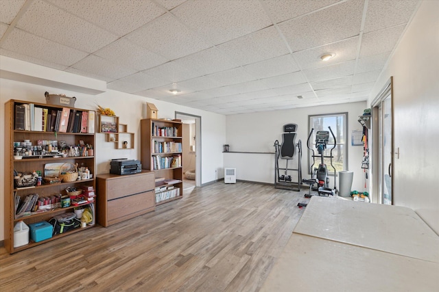 workout room featuring light wood-style flooring, a paneled ceiling, and baseboards