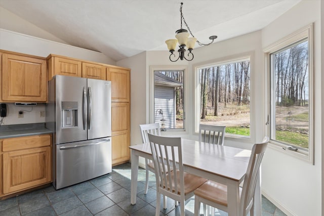 kitchen with stainless steel fridge, an inviting chandelier, dark countertops, dark tile patterned flooring, and lofted ceiling
