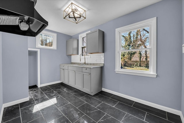 kitchen with a sink, gray cabinets, light countertops, baseboards, and ventilation hood