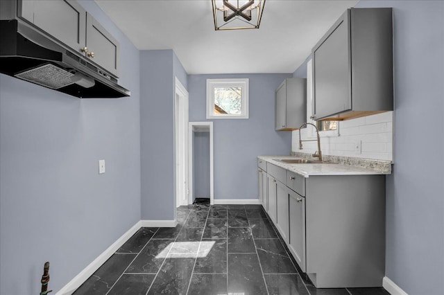 kitchen featuring baseboards, under cabinet range hood, a sink, and gray cabinets