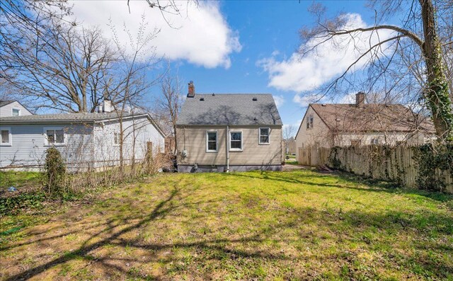 rear view of house with a yard, a chimney, and fence