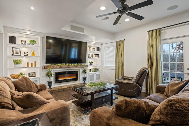 living area featuring wood finished floors, a glass covered fireplace, visible vents, and built in features