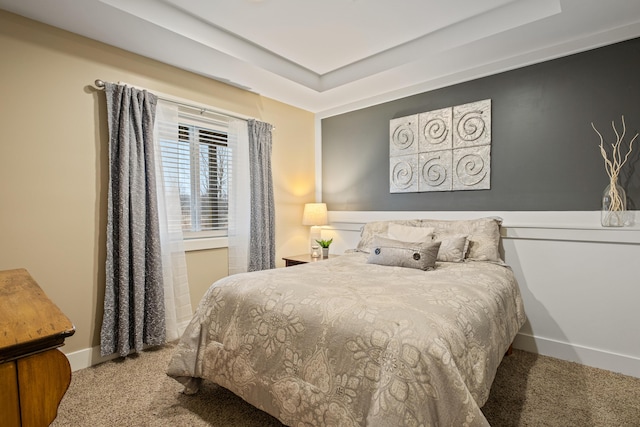 carpeted bedroom with a raised ceiling and baseboards