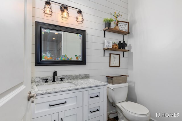 bathroom featuring wooden walls, toilet, and vanity