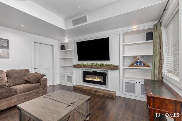 living room with dark wood finished floors, visible vents, built in shelves, and a glass covered fireplace