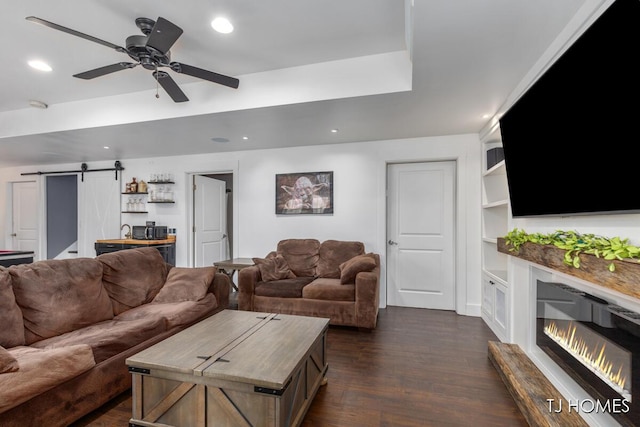 living area featuring a barn door, dark wood-style flooring, ceiling fan, recessed lighting, and a glass covered fireplace