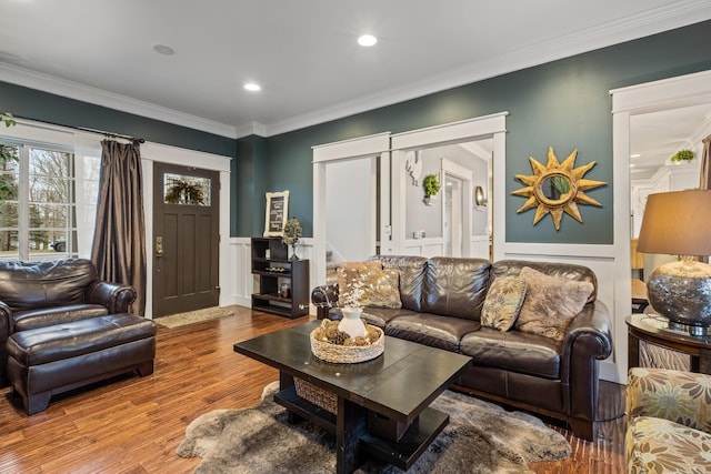 living area with crown molding, a decorative wall, recessed lighting, wood finished floors, and wainscoting