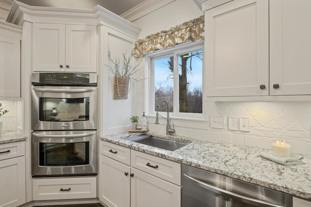 kitchen featuring tasteful backsplash, white cabinets, appliances with stainless steel finishes, light stone counters, and a sink
