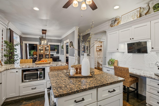 kitchen with crown molding, light stone counters, stainless steel microwave, and backsplash