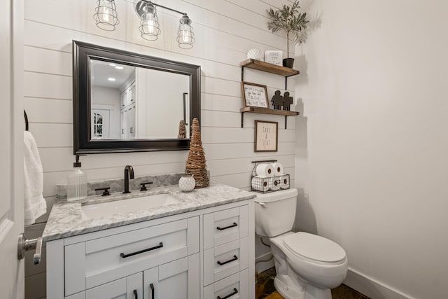 half bath with wood walls, toilet, vanity, and baseboards