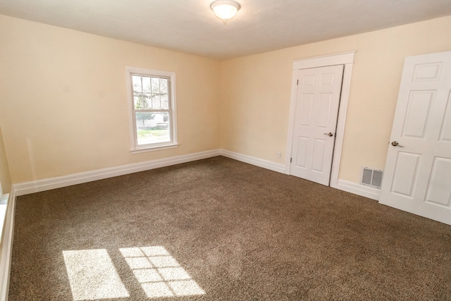 unfurnished room featuring dark colored carpet, visible vents, and baseboards