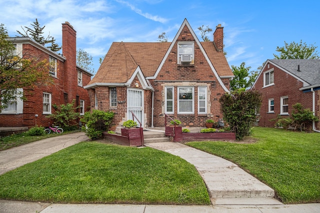 tudor-style house with a chimney, a front yard, and brick siding