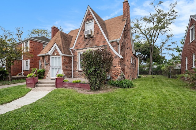 tudor home with brick siding, a chimney, and a front yard