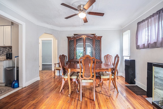 dining area with arched walkways, light wood finished floors, a ceiling fan, crown molding, and baseboards