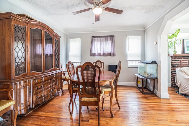 dining area featuring a textured ceiling, light wood-style floors, ceiling fan, crown molding, and baseboards