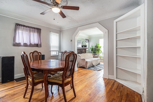 dining area featuring light wood-style flooring, arched walkways, built in features, ornamental molding, and a ceiling fan