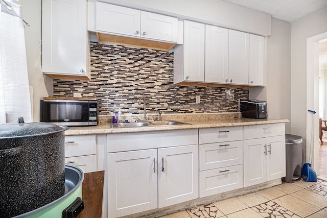 kitchen featuring a sink, stainless steel microwave, backsplash, white cabinetry, and light countertops