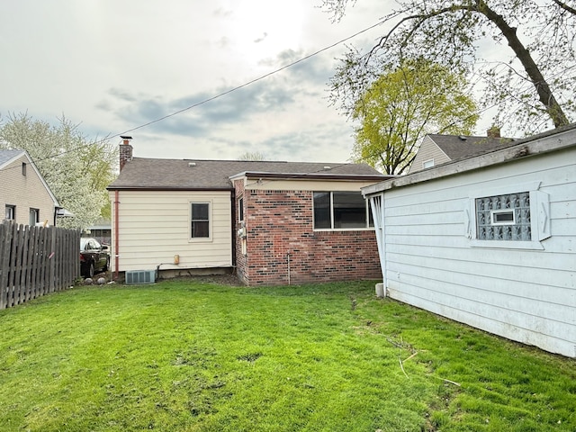 rear view of property featuring fence, a chimney, a yard, and brick siding