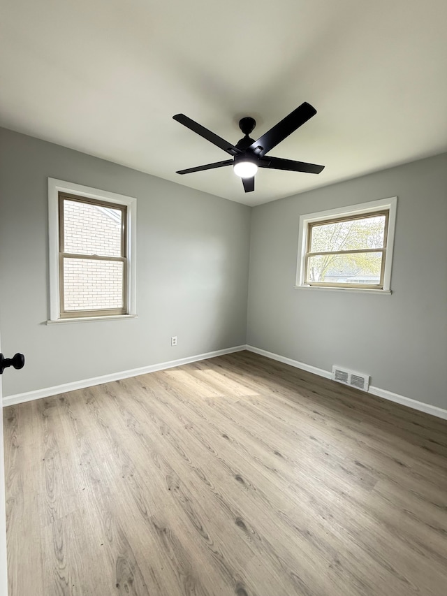 empty room with wood finished floors, visible vents, a ceiling fan, and baseboards