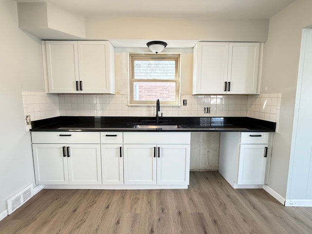 kitchen with white cabinetry, a sink, dark countertops, visible vents, and light wood-type flooring