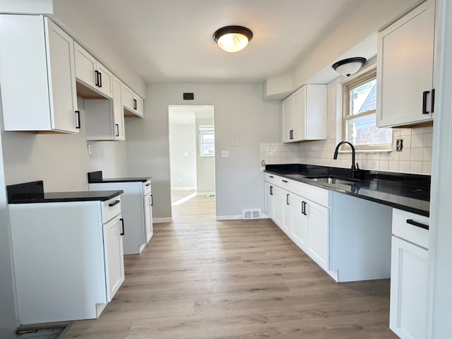 kitchen featuring light wood finished floors, a sink, tasteful backsplash, visible vents, and dark countertops