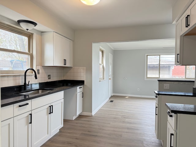 kitchen with decorative backsplash, a sink, baseboards, light wood-type flooring, and a wealth of natural light
