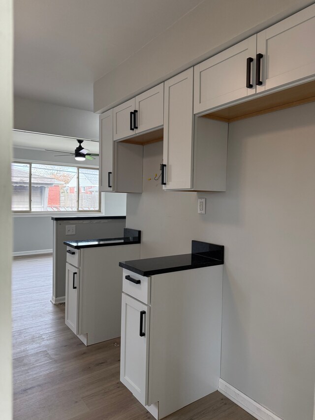 kitchen with white cabinetry, dark countertops, baseboards, wood finished floors, and a ceiling fan