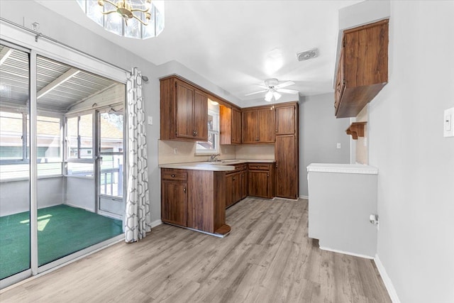 kitchen with brown cabinets, light countertops, light wood-type flooring, and ceiling fan with notable chandelier