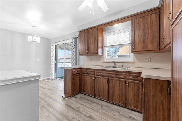 kitchen featuring a sink, light countertops, pendant lighting, light wood-style flooring, and a peninsula