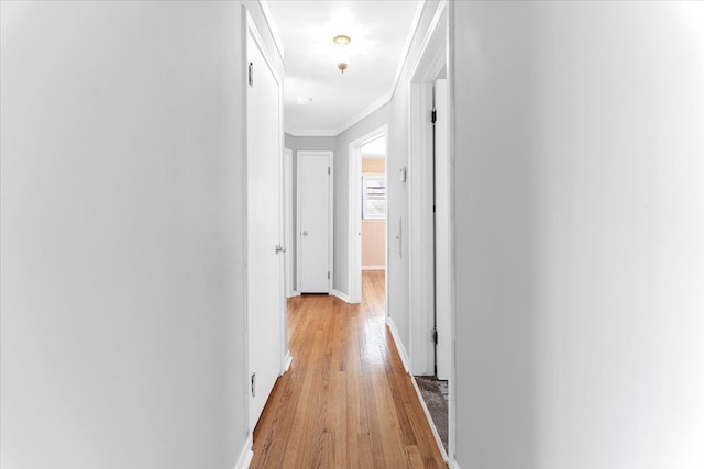 corridor featuring baseboards, crown molding, and light wood finished floors