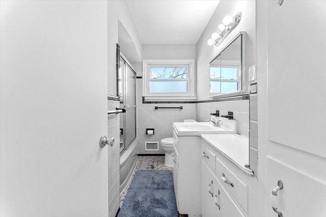 full bathroom featuring visible vents, toilet, vanity, tile walls, and bath / shower combo with glass door