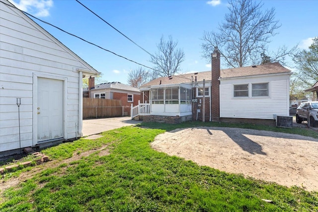 back of property with central air condition unit, a chimney, fence, a yard, and a sunroom